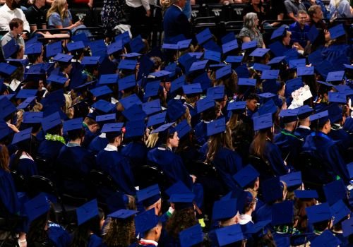 Đám đông sinh viên tốt nghiệp với mũ áo cử nhân màu xanh – biểu tượng của khủng hoảng bằng cấp trong xã hội hiện đại, thúc đẩy nhu cầu hợp tác kinh doanh để tạo giá trị thực.